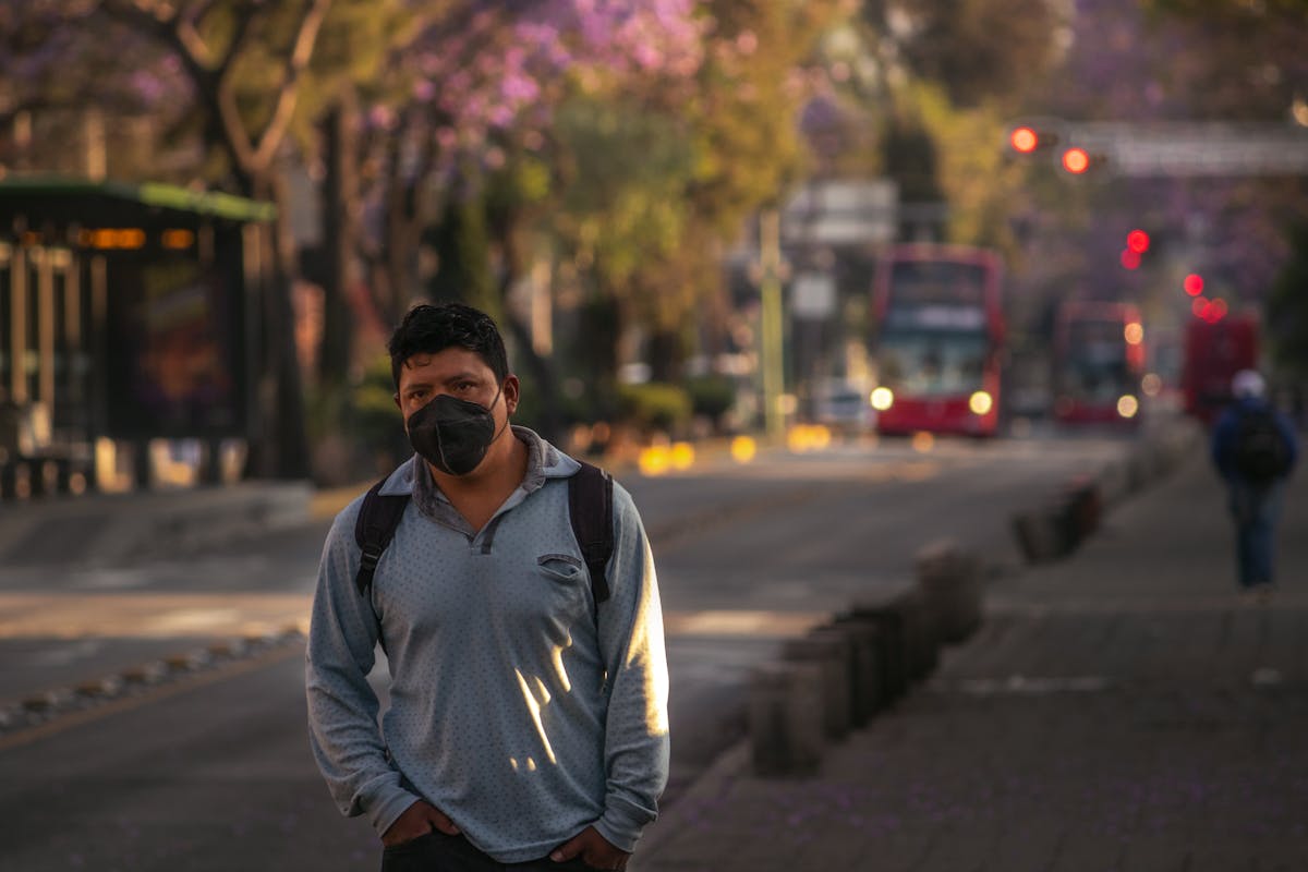 a man in gray long sleeves wearing face mask while walking on the side of the road