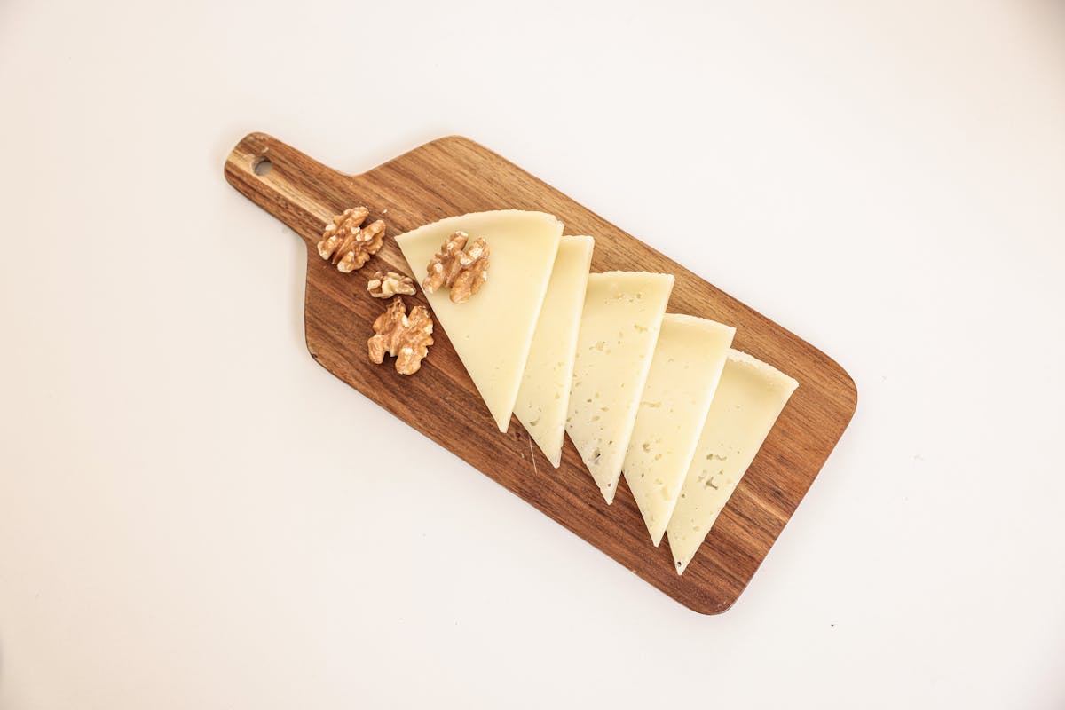 a sliced cheese and walnuts on a wooden board