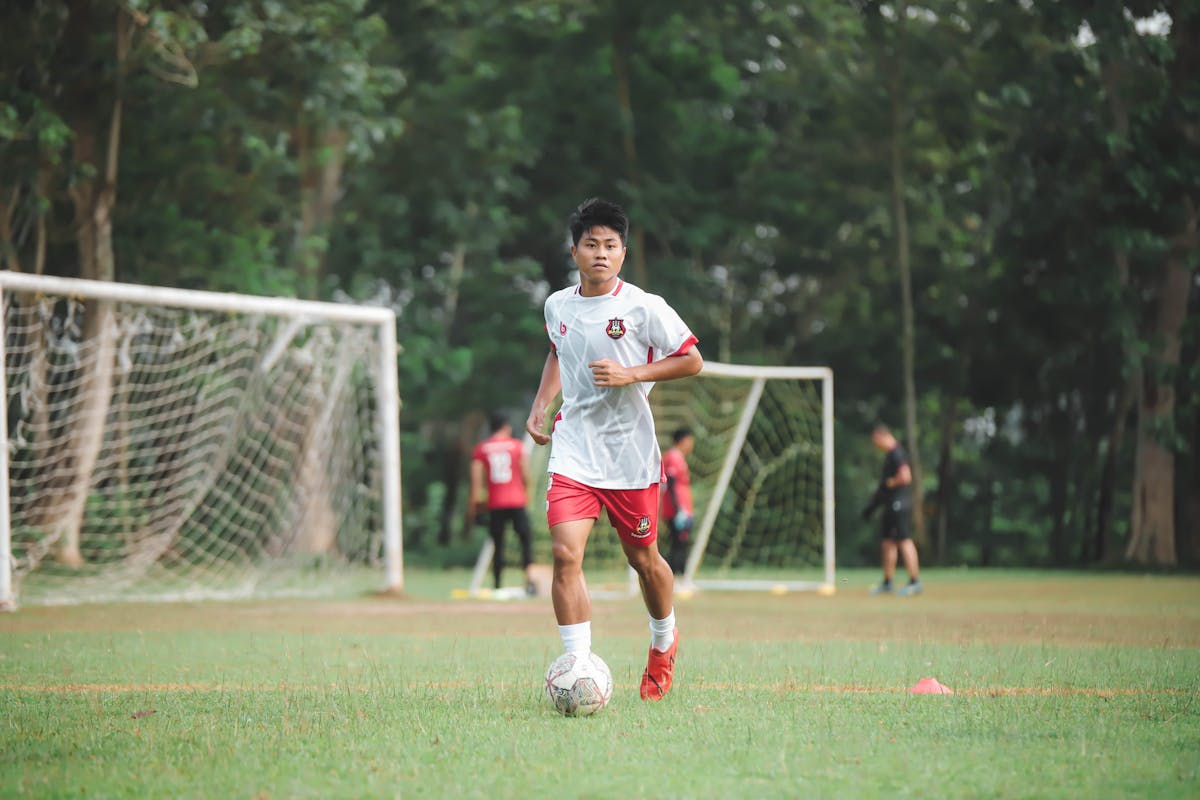 a young man in red and white soccer uniform kicking a soccer ball