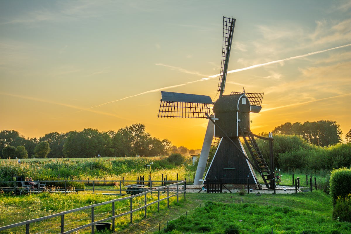 black and white wind mill in green field under yellow skies black and white wind mill in green field under yellow skies