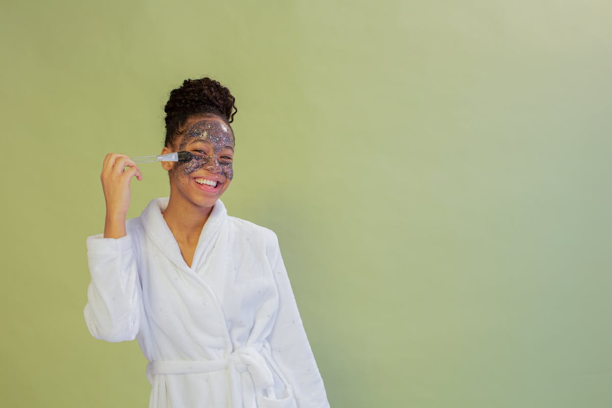 cheerful black teen applying scrub mask on face