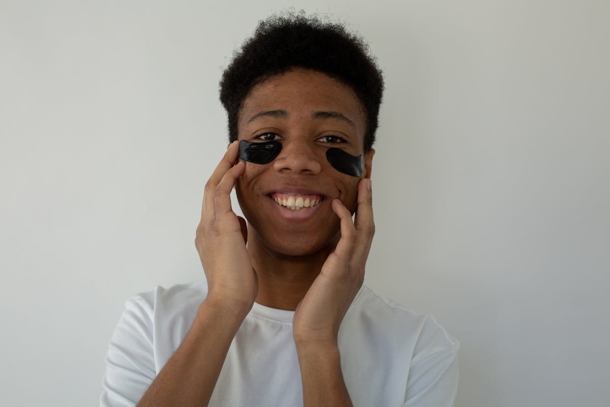 cheerful black teenager touching face with eye patches
