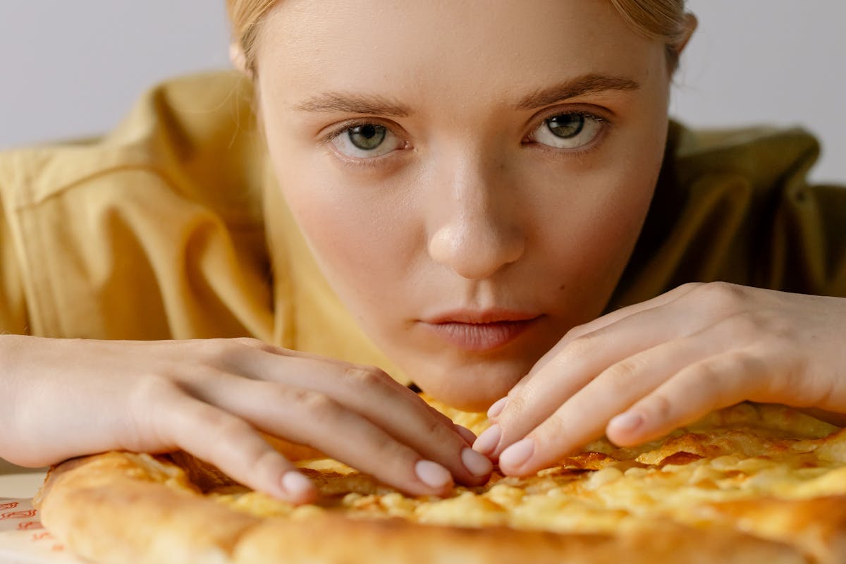 close up shot of a woman in yellow long sleeves holding the pizza