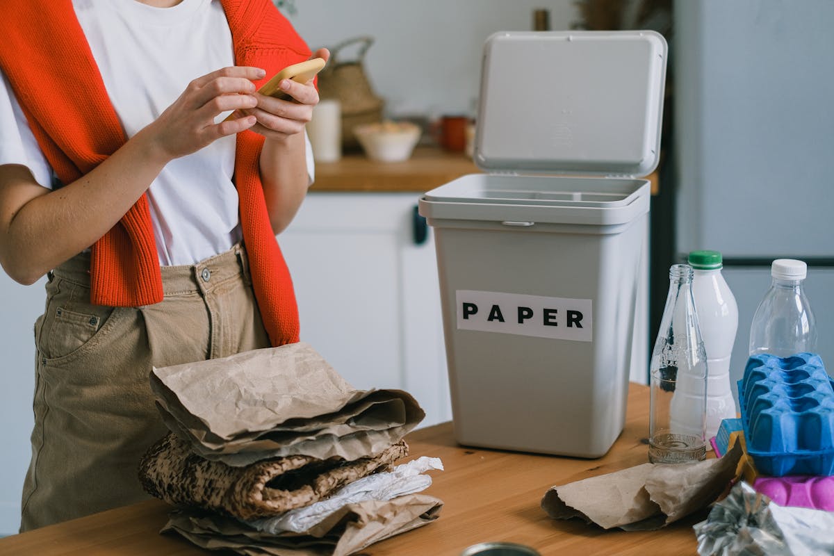 crop person browsing cellphone while sorting waste