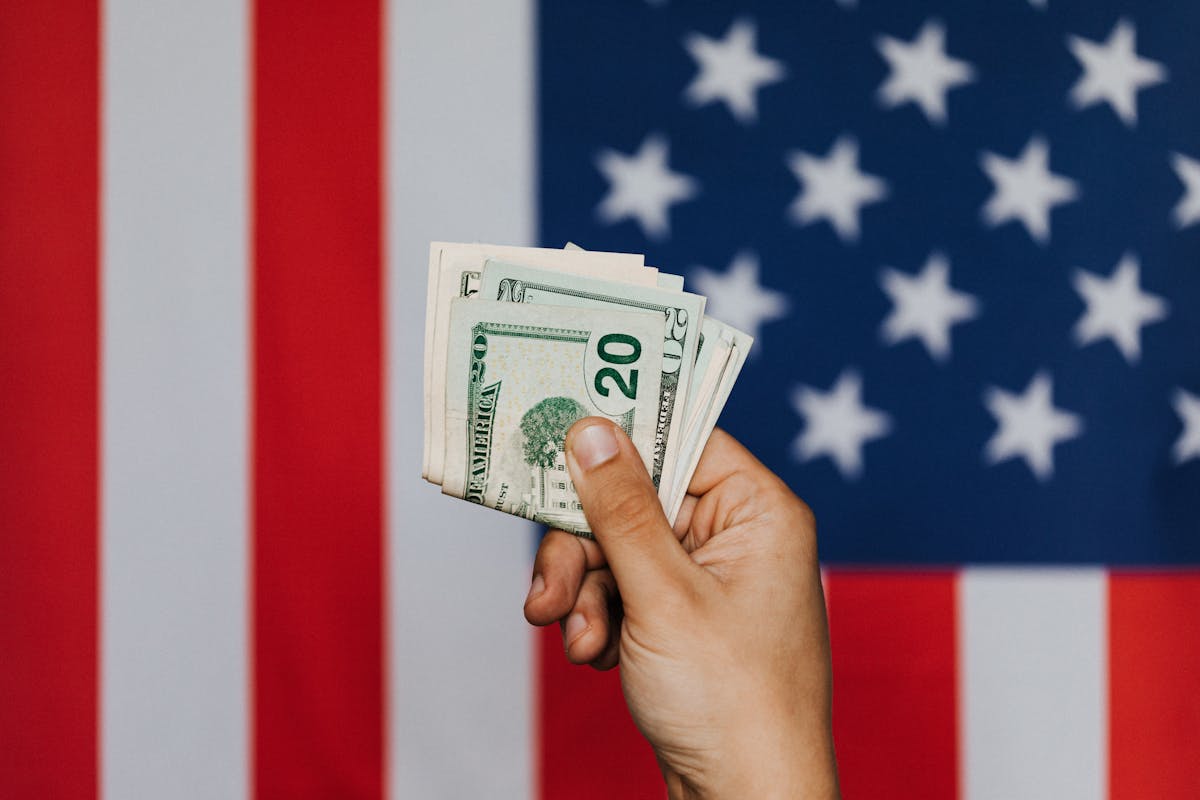 crop person showing pack of dollars against american flag