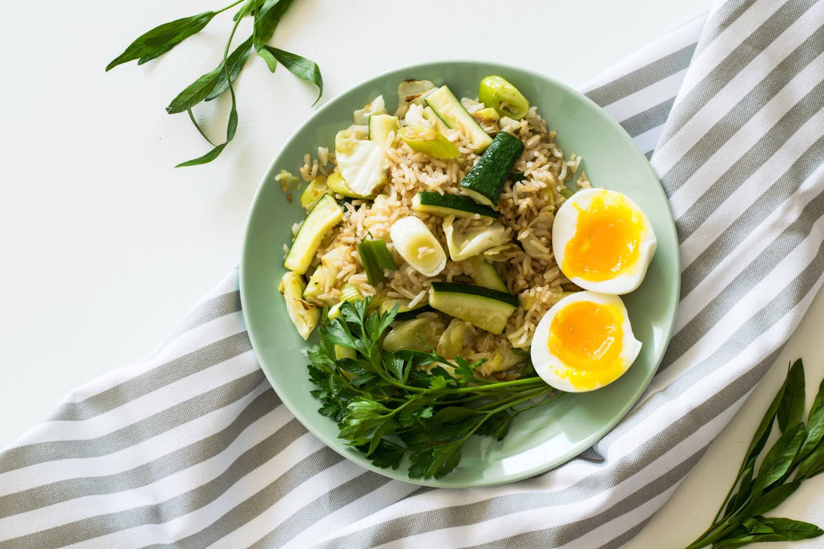 fried rice with poached egg zucchini and celery on round green ceramic plate