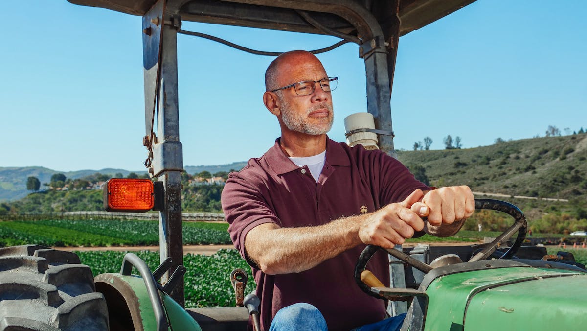 man in maroon shirt driving a tractor