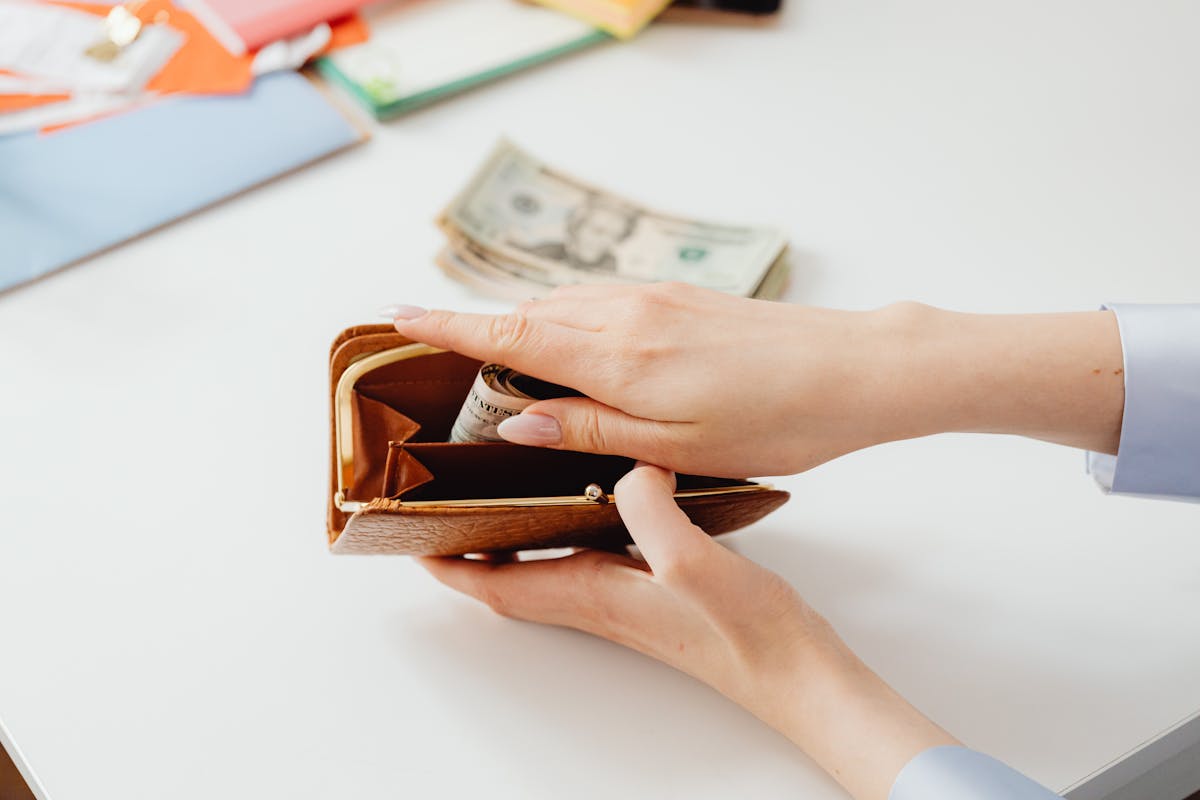 person putting money in a brown wallet