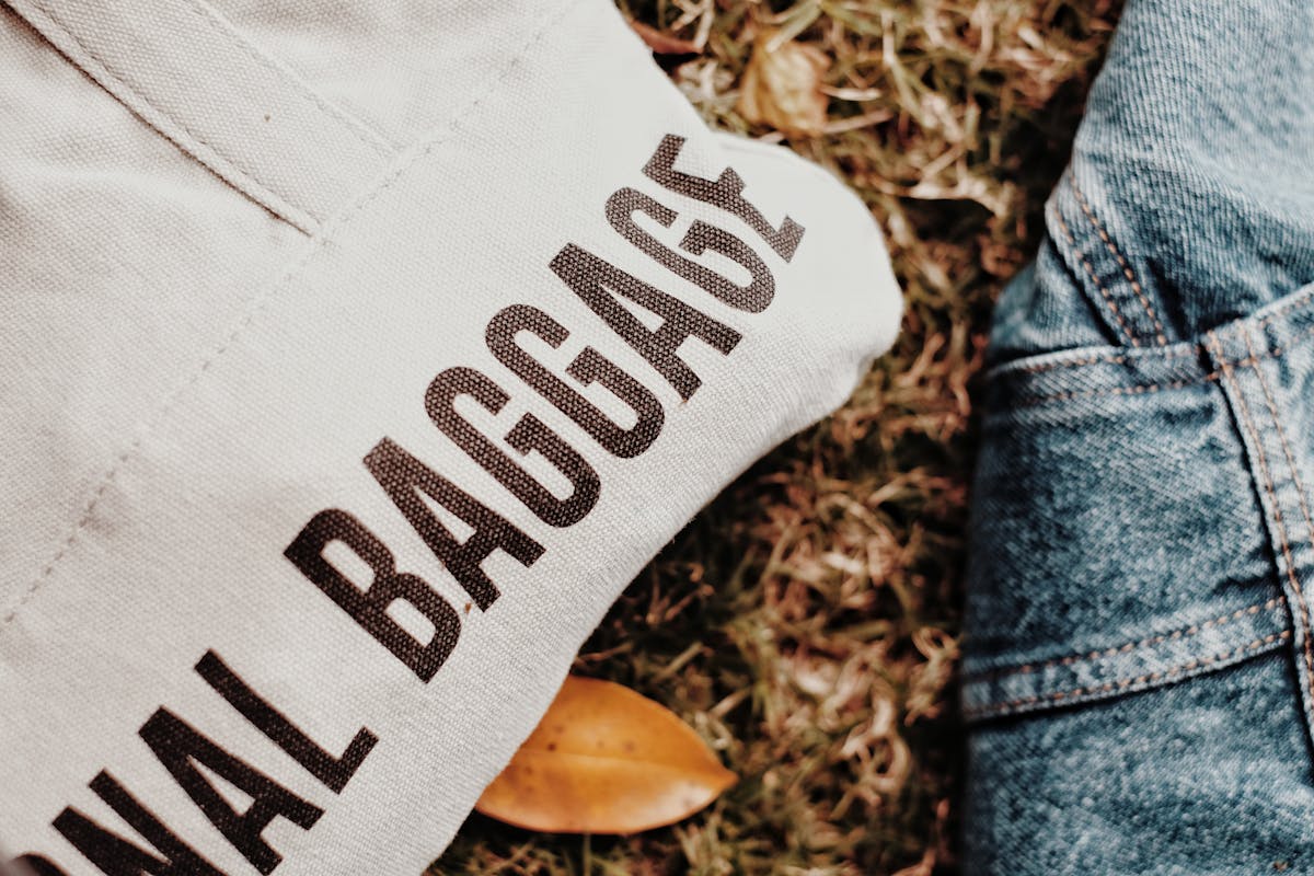 shopping bag with printed baggage text beside denim jacket on grass