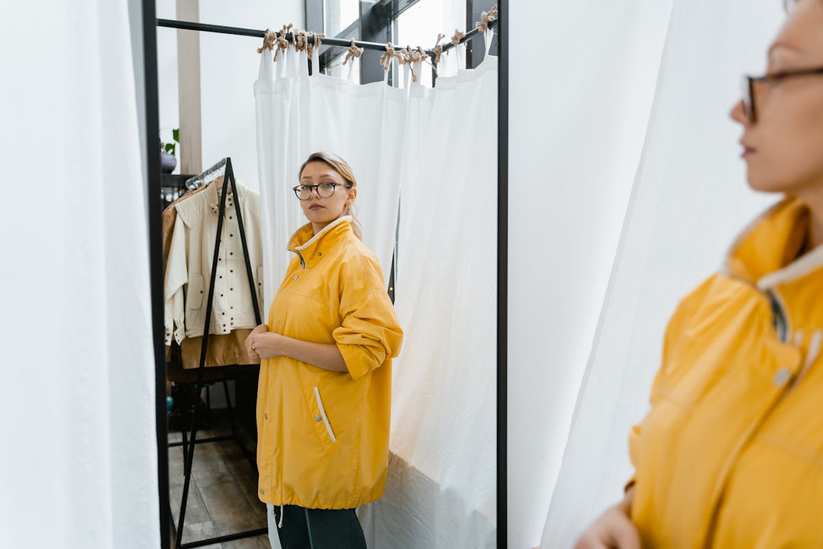 woman in yellow jacket standing in front of a mirror